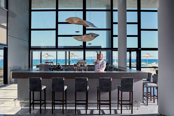 Ein Barkeeper im Sentido Unique Blue Resort & Villas serviert Getränke an der Bar mit Blick auf den Ozean.