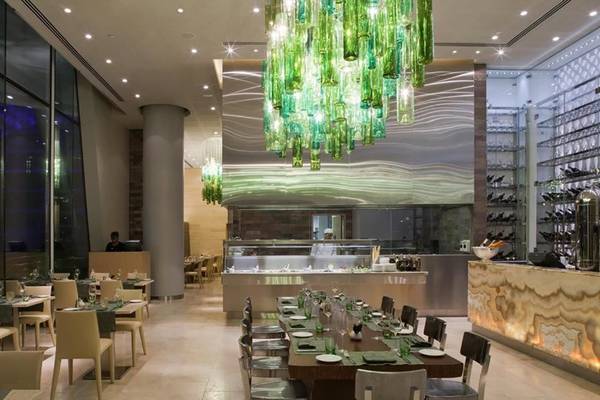 Innenansicht des Restaurants im W Abu Dhabi auf Yas Island mit grüner Kronleuchter und langen Esstischen.