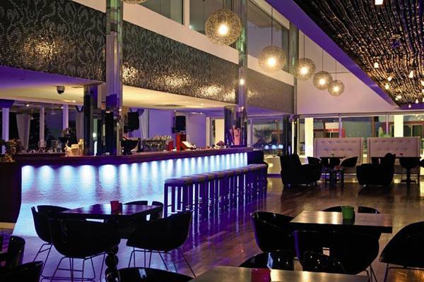 Innenansicht der Bar im Napa Mermaid Hotel & Suites mit lila Beleuchtung, Thekenhockern und runden Tischen.