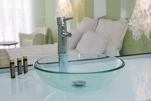 Glasbecken im Badezimmer des Napa Mermaid Hotels mit Chromhahn und grünem Hintergrund.