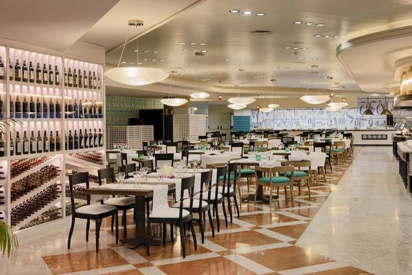 Innenansicht des Restaurants im H10 Timanfaya Palace Hotel mit gedeckten Tischen, Weinflaschen an der Wand und Kronleuchtern.