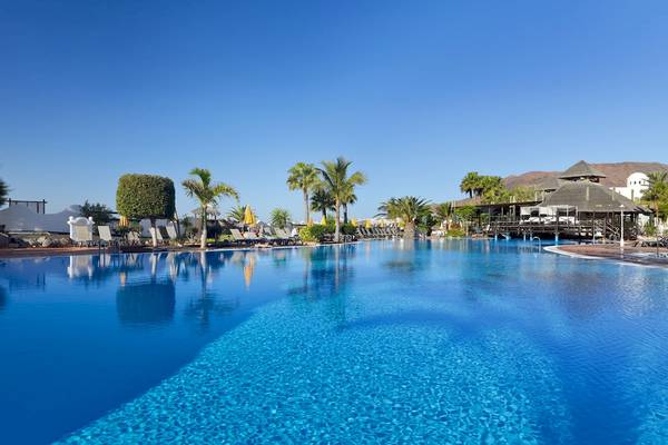 Außenpool des H10 Timanfaya Palace Hotels mit Lounge-Sesseln und Sonnenschirmen.