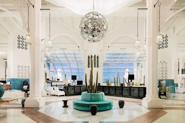 Innenansicht der Lobby des H10 Timanfaya Palace mit zentralem Kaktus in blauem Topf und Spiegel-Pendelleuchte.