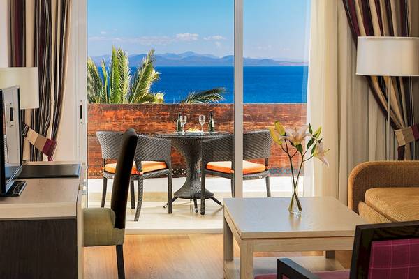 Aussicht von einem Zimmer im H10 Timanfaya Palace Hotel auf das Meer und eine Terrasse mit Tisch und Stühlen.