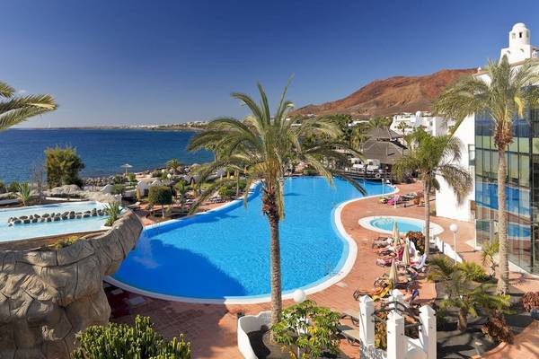 Außenbereich des H10 Timanfaya Palace mit zwei Swimmingpools und Sonnenliegen.