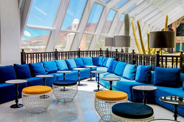 Loungebereich des H10 Timanfaya Palace Hotels mit blauen Sofas, orangen Hockern und Tischen.