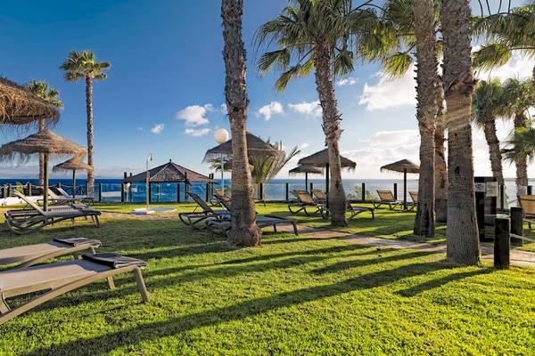 Das H10 Timanfaya Palace Hotel mit Liegestühlen und Sonnenschirmen am Strand.