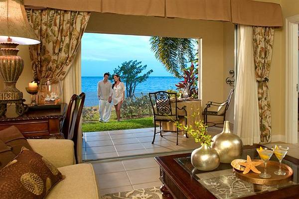 Wohnbereich des Sandals Whitehouse European Village & Spa mit Blick auf das Meer, zwei Personen stehen auf der Terrasse