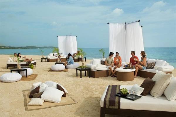 Gäste entspannen sich auf Loungemöbeln am Strand im Sandals Whitehouse European Village & Spa.