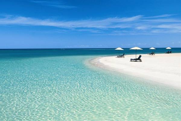 Strand mit weißen Sonnenliegen und Sonnenschirmen im Wasser
