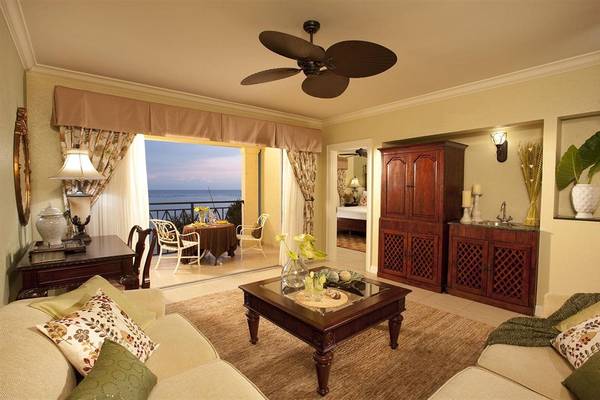 Wohnzimmer mit Aussicht auf das Meer, inklusive Sofa, Tisch, Fenster und Deckenventilator.