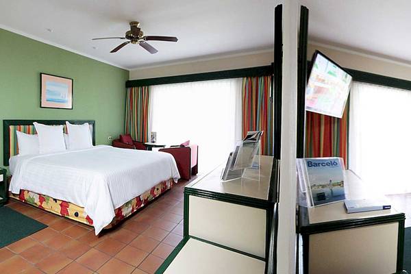 Zimmer im Barcelo Tambor Hotel mit einem Bett, einem Fernseher, einem Ventilator und einem Tisch.