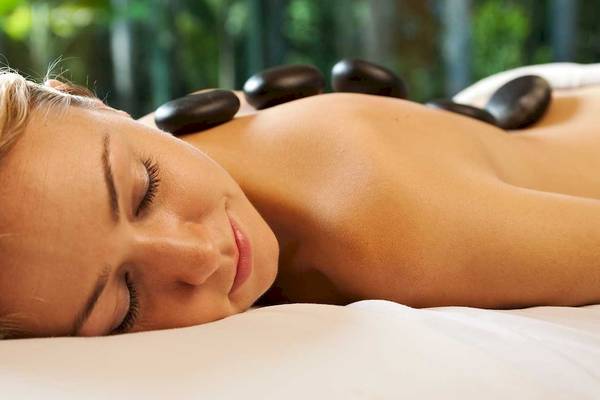 Eine Frau genießt eine Massage im Spa, mit Steinen auf dem Rücken liegend.
