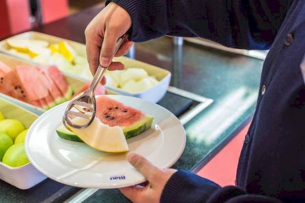 Eine Hand schneidet eine Wassermelone auf einem Teller im Buffet.