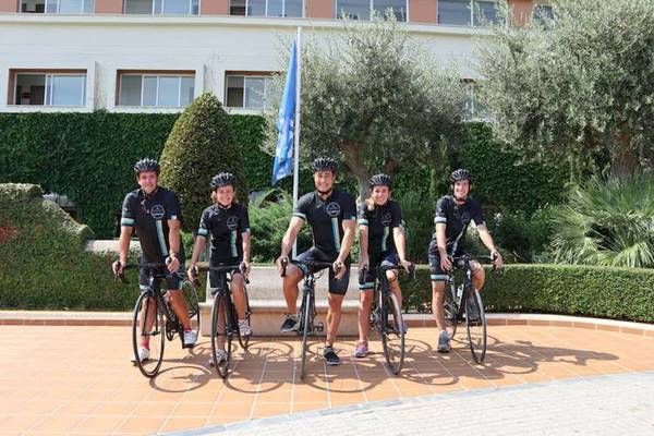 Gruppe von Radfahrern vor dem Blau Punta Reina Hotel, alle in Radsporttrikots gekleidet.