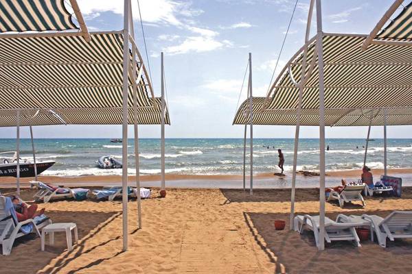 Sonnenschirme am Strand des Sunis Kumköy Beach Resort & Spa mit Gästen und einem Boot im Hintergrund.