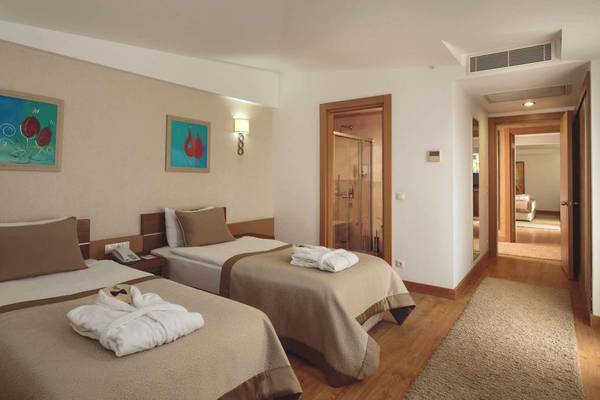 Zwei Betten in einem Hotelzimmer des Sunis Kumköy Beach Resort & Spa mit weißen Decken, Kissen und Bademänteln.