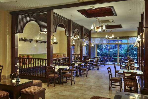 Innenansicht des Restaurants im Sunis Kumköy Beach Resort & Spa mit braunen Holzmöbeln, Kronleuchtern und Blick auf den Garten.