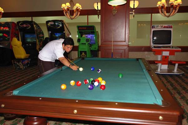 Ein Mann spielt Billard in einem Spielzimmer mit Arcade-Spielen im Hintergrund.