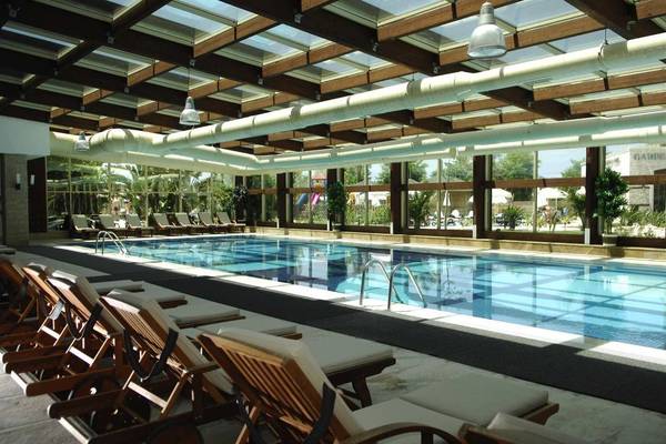Das Hallenbad des Sunis Kumköy Beach Resort & Spa mit braunen Liegestühlen und einer Glasdecke.