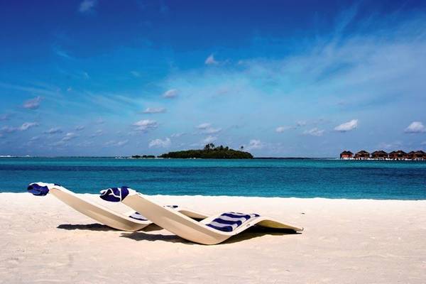 Zwei Sonnenliegen auf einem weißen Sandstrand mit blauem Himmel und Meer im Hintergrund, vor dem Hotel Cinnamon Dhonveli Maldives.
