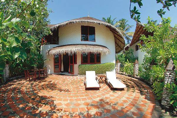 Villa im Cinnamon Dhonveli Maldives mit einem gepflasterten Vorgarten und zwei weißen Liegestühlen.