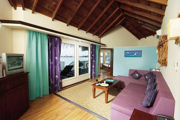 Innenbereich eines Hotelzimmers mit einer violetten Couch, einem Fernseher, einem Tisch, einem Teppich und einem Blick auf den Ozean.