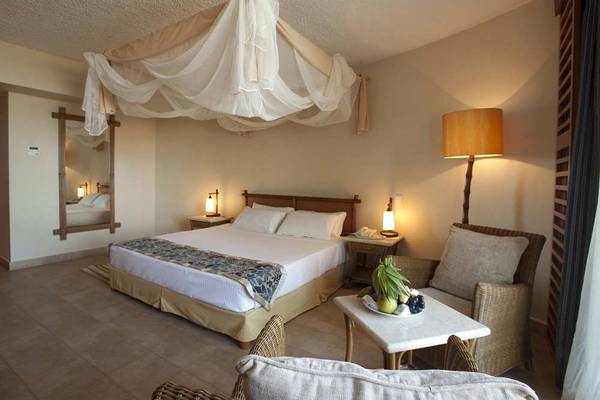Zimmer im Bahari Beach Hotel mit Doppelbett, Moskitonetz, Lampen und Möbeln.