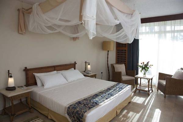 Schlafzimmer im Bahari Beach Hotel mit Bett, Nachttischen, Stühlen und Fenstern.