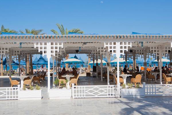 Außenterrasse des Grand Hotel Hurghada mit blauen Sonnenschirmen und Tischen im Freien.