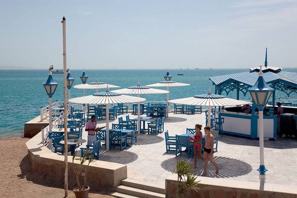 Außenterrasse des Grand Hotel Hurghada mit Blick auf das Meer und mehreren blauen Sonnenschirmen.