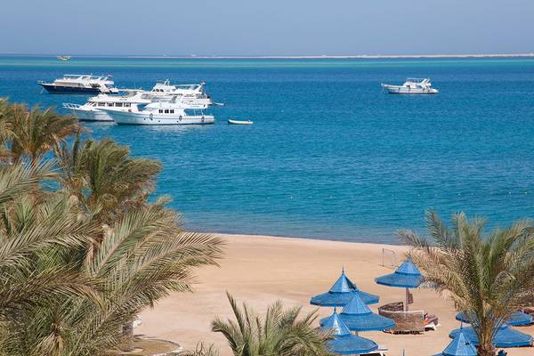 Strandansicht des Grand Hotel Hurghada mit weißen Booten im Meer und blauen Sonnenschirmen