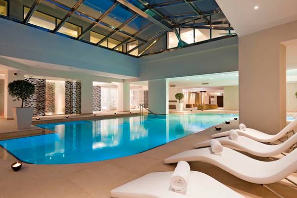 Innenpool des Porto Platanias Beach Resort & Spa mit weißen Sonnenliegen und einem großen Glasdach.
