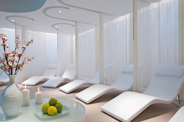 Entspannungsbereich im Porto Platanias Beach Resort & Spa mit weißen Liegen, Tisch, Früchten und Kerzen.