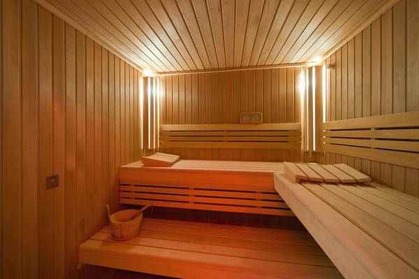 Innenansicht einer Holzsauna im Porto Platanias Beach Resort & Spa mit zwei Holzbänken und einem Eimer.