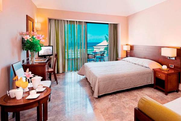 Zimmer im Porto Platanias Beach Resort mit Blick auf das Meer und eine Terrasse mit Tisch und Stühlen.