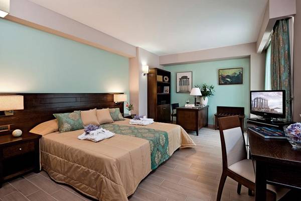 Porto Platanias Beach Resort Zimmer mit Bett, Schreibtisch und Fernseher.