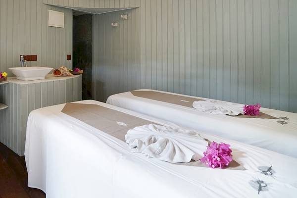 Massage-Behandlungsraum im Nika Island Resort & Spa mit zwei Behandlungstischen, einem Waschbecken und Blumendekoration.
