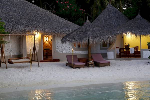 Hutten des Nika Island Resorts & Spa am Strand mit Loungestühlen und Sonnenschirm.