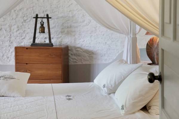 Ein Schlafzimmer im Nika Island Resort & Spa mit einem Bett, weißen Laken und Kissen, einem Nachttisch und einer Wand mit einem Lampenständer.