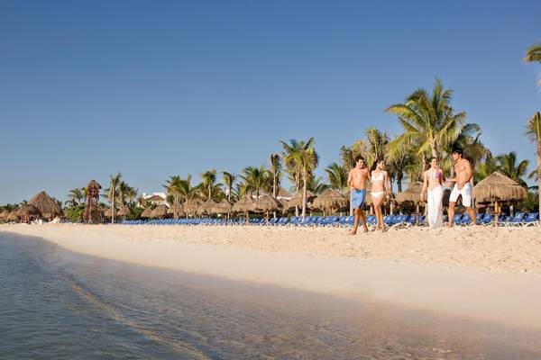 Strand mit mehreren Personen, die auf dem weißen Sandstrand des Grand Sunset Princess All Suites Resorts spazieren.