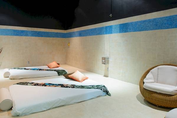 Massageraum im Grand Sunset Princess All Suites Resort mit zwei Betten, Kissen und einer Korbsessel.