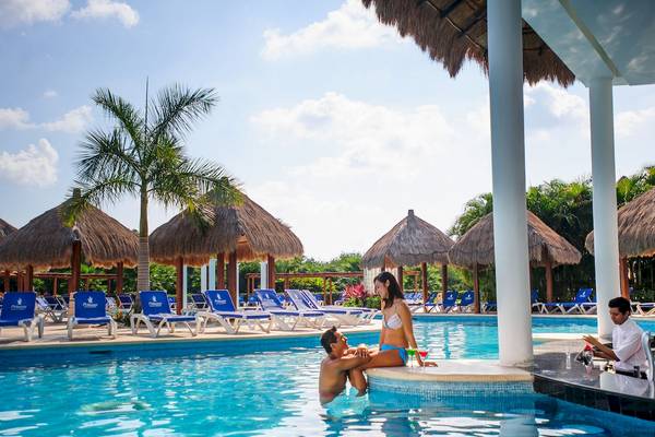 Paar am Poolrand im Grand Sunset Princess All Suites Resort, mit Barkeeper im Hintergrund.