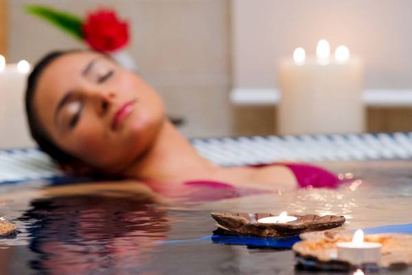 Eine Frau schläft in einer Badewanne mit Kerzen und Blumen.