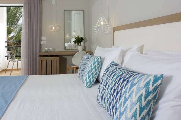 Bett im Paradise Hotel Corfu mit blauen Kissen und weißem Bettlaken.