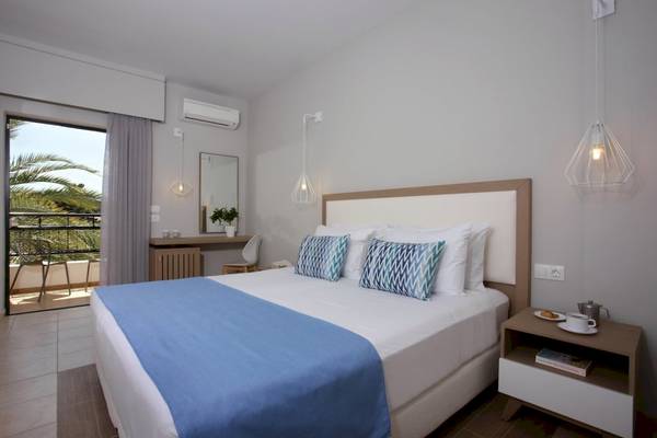 Ein modernes Hotelzimmer im Paradise Hotel Corfu mit Bett, Nachttisch und Balkonzugang.