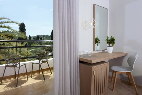 Ein modernes Zimmer im Paradise Hotel Corfu mit einem Schreibtisch, Stühlen und einem Balkon mit Blick auf die Natur.