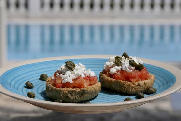 Zwei Tartine mit Tomaten und Feta auf einem blauen Teller mit einem Pool im Hintergrund.