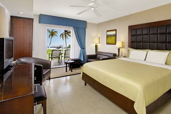 Hotelzimmer mit Balkon im Divi Tamarijn Aruba, inklusive Bett, Fernseher, Tisch, Stühle und Meerblick.