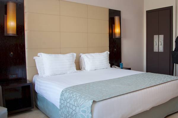 Ein Hotelzimmer im Bianca Beach Resort mit einem Doppelbett, zwei weißen Kissen, zwei Wandleuchten und einer Tür.